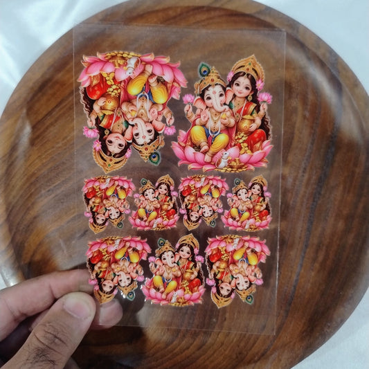 A sheet of colorful 3D Laxmi Ganesha UV DTF transfer stickers on lotus flowers held over a wooden plate for resin art and candle jar crafts.