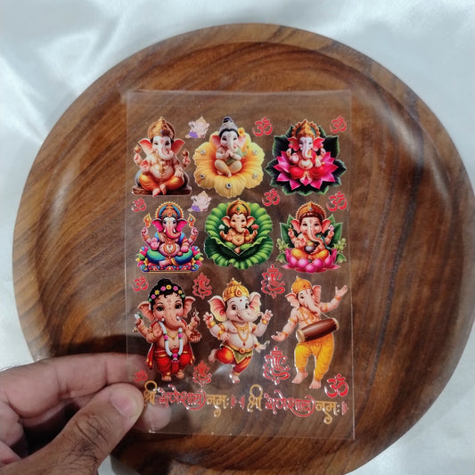 A sheet of 3D colorful Lord Ganesha UV DTF transfer stickers on lotus flowers with Shree Ganeshay Namah text held over a wooden plate.