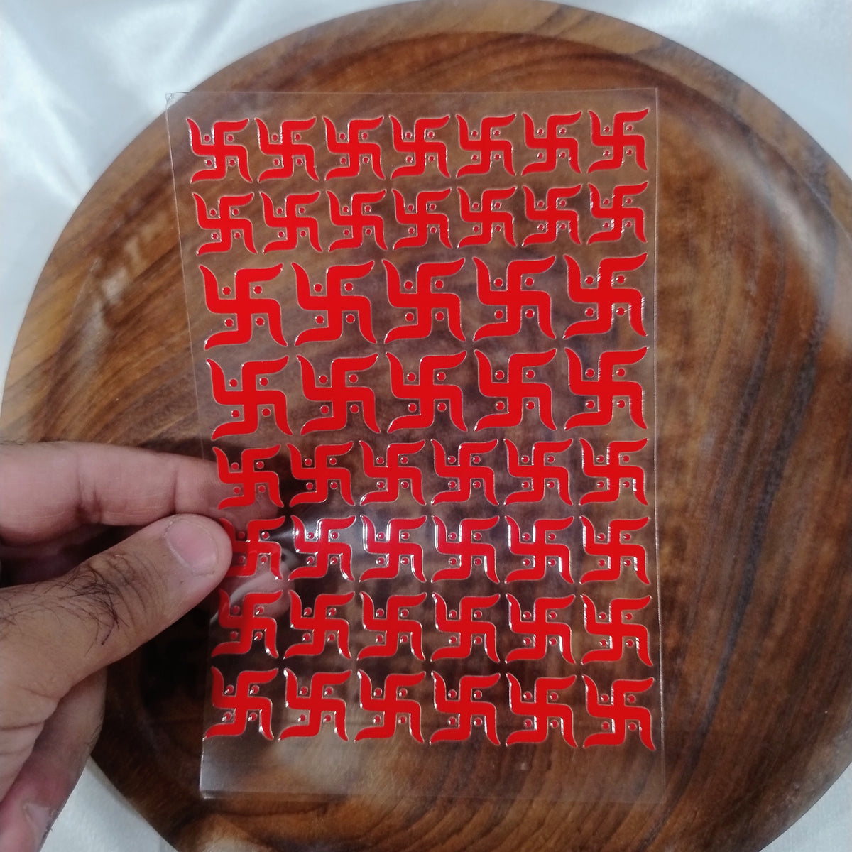 A sheet of 3D glossy red Swastik UV DTF transfer stickers in multiple sizes held over a wooden plate for resin art and festive crafts.